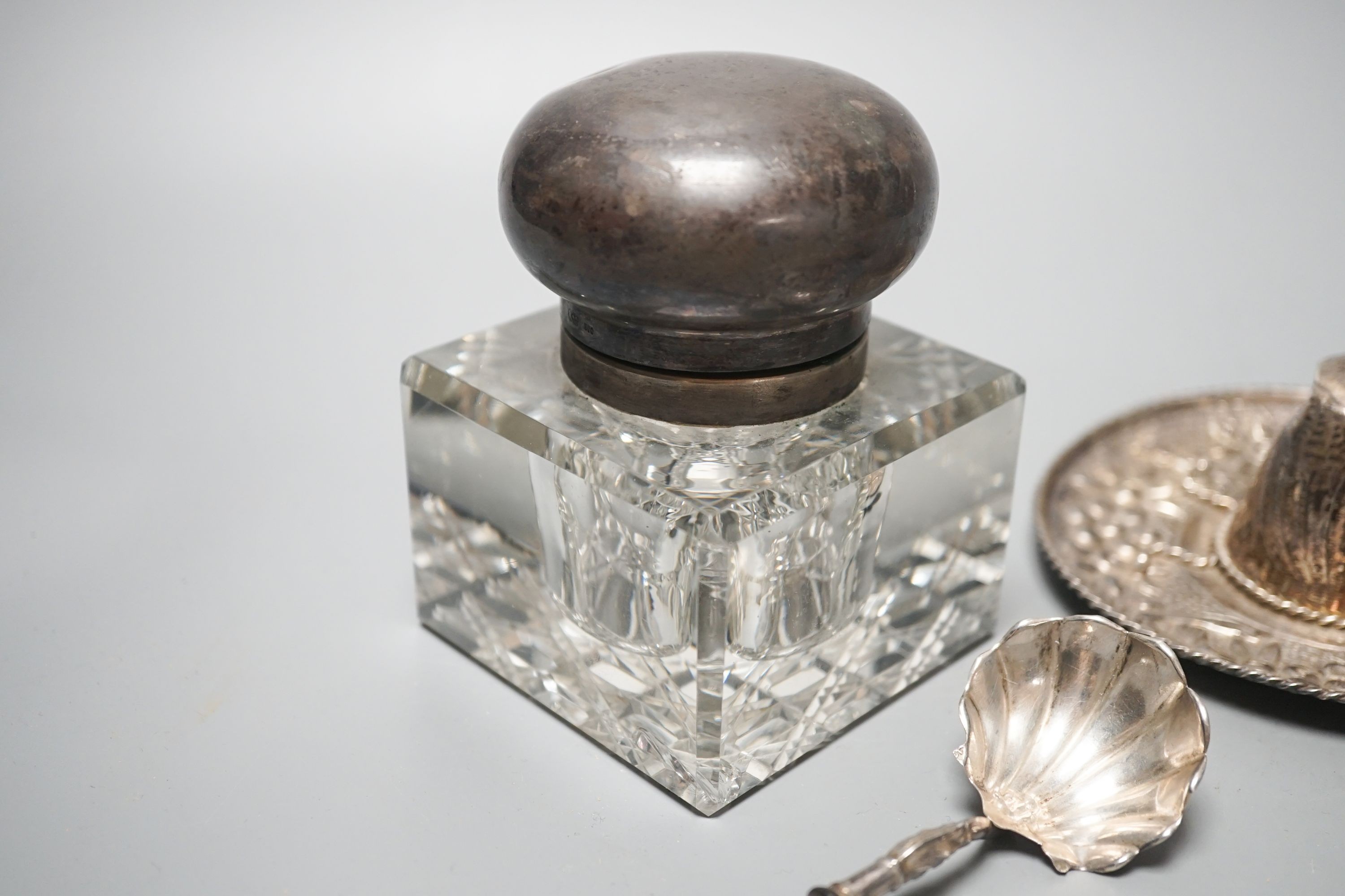 A silver mounted glass inkwell, A Mexican white metal miniature sombrero, a white metal caddy spoon and a filigree horse and carriage.